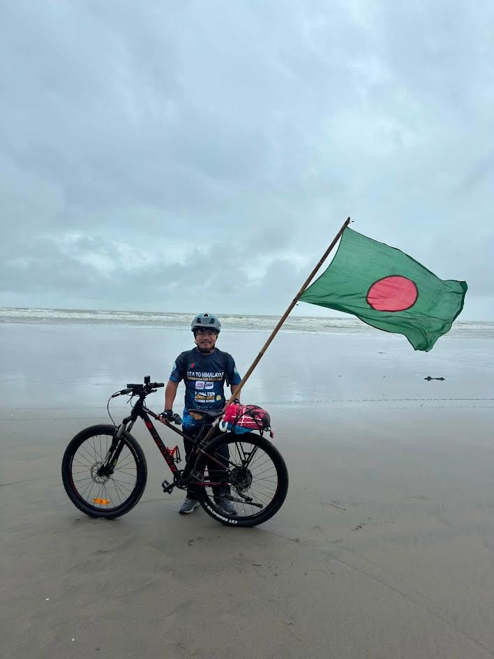 কক্সবাজার সমুদ্রসৈকতে সাইকেল ও বাংলাদেশের পতাকাসহ তরুণ অভিযাত্রী বীর কুমার তঞ্চঙ্গ্যা।